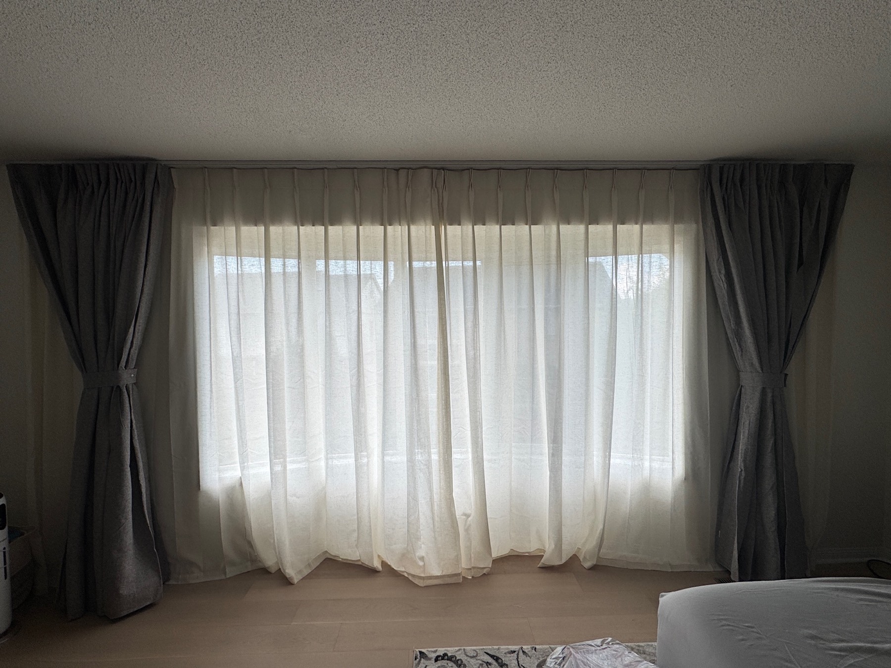 Pinch-pleat drapery panels layered over sheers on a ceiling-mounted bedroom track